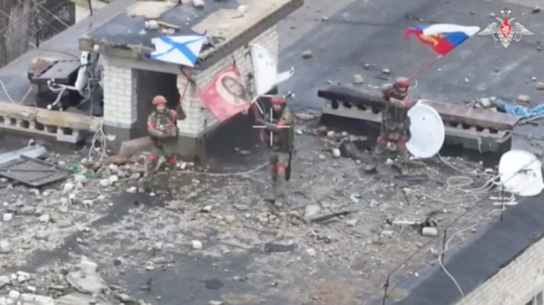 Russian service members wave flags on the roof of a building in Velyka Novosilka